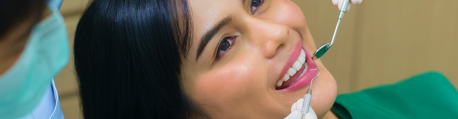 Gloved hands using dental tools in woman's mouth.
